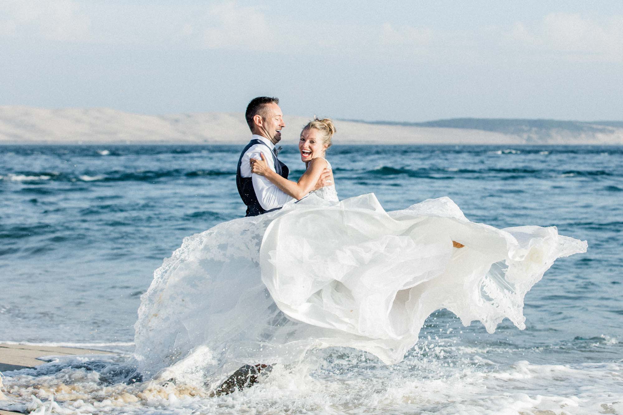 Mariés dans les vagues, robe soulevée par l'écume, séance trash the dress au Cap Ferret