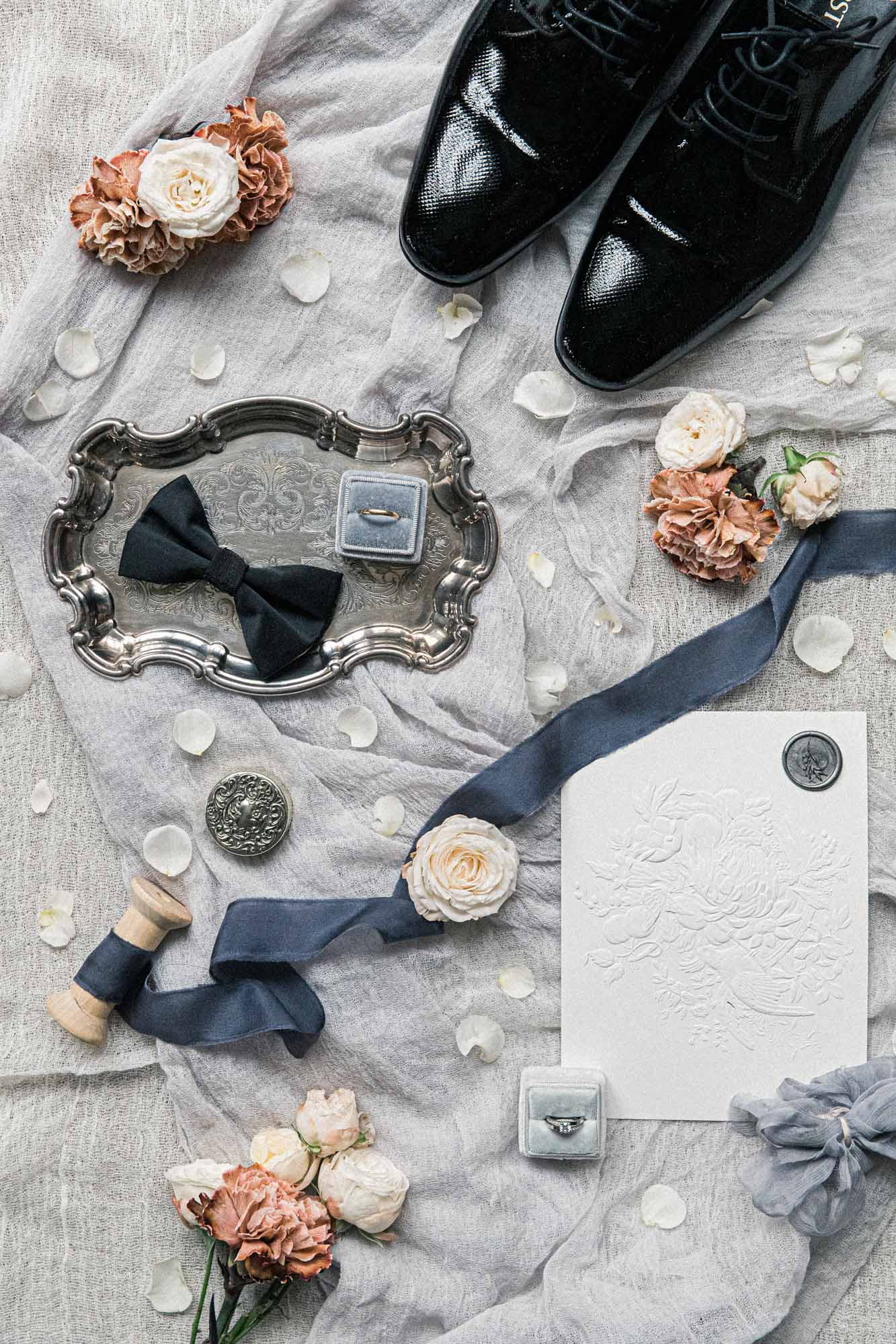 Flat lay du marié : chaussures vernies, nœud papillon, écrin et fleurs séchées