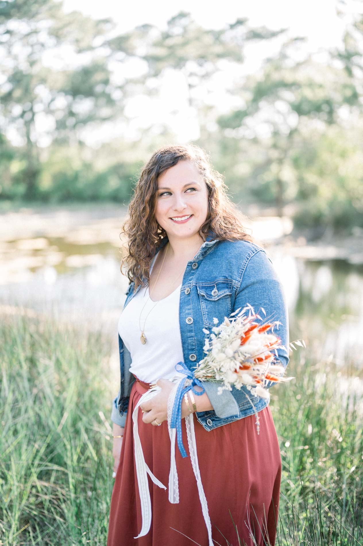 Femme souriante en veste en jean tenant un bouquet dans les herbes hautes