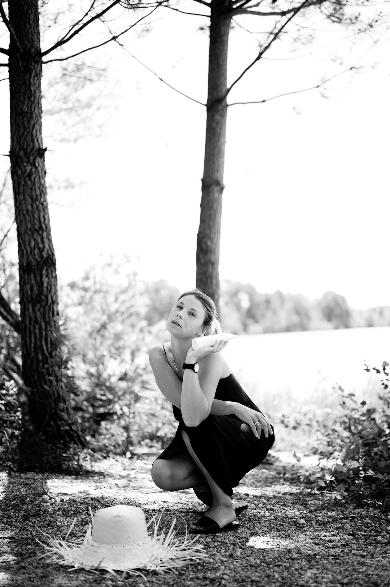 Mannequin accroupie au bord de l'eau, chapeau de paille au sol, en noir et blanc