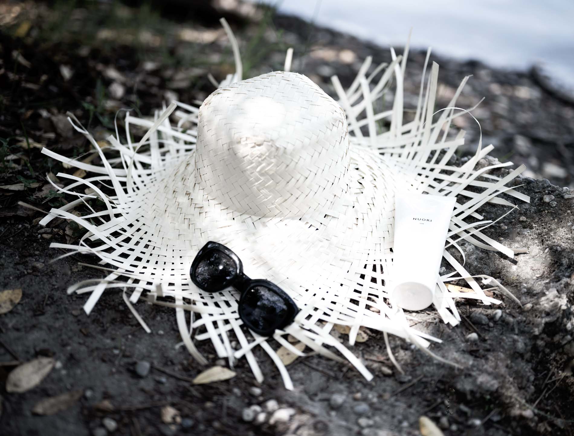 Chapeau de paille, lunettes de soleil et crème Nuori posés sur la terre