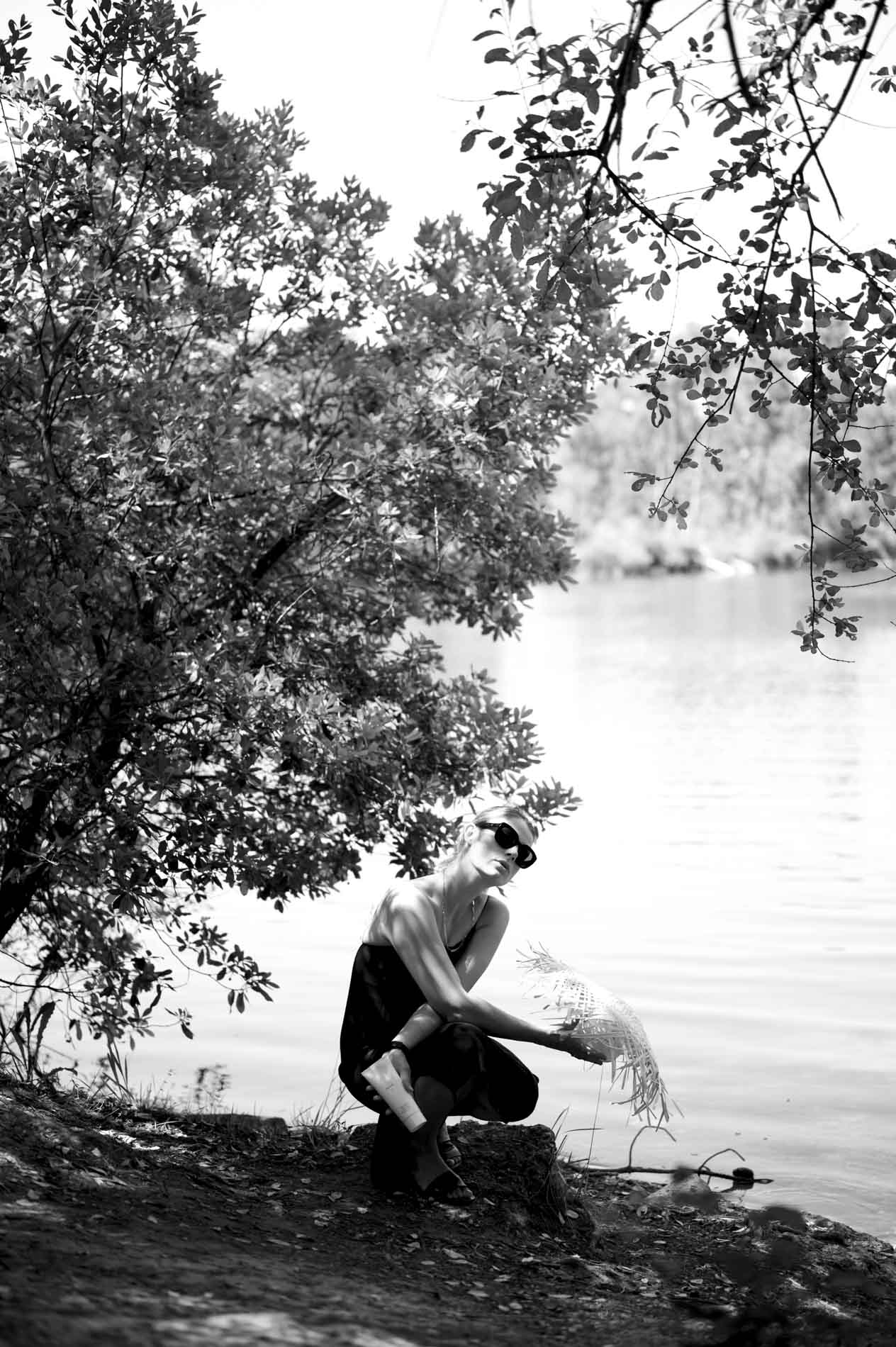 Mannequin accroupie sous un arbre au bord d'un lac, en noir et blanc
