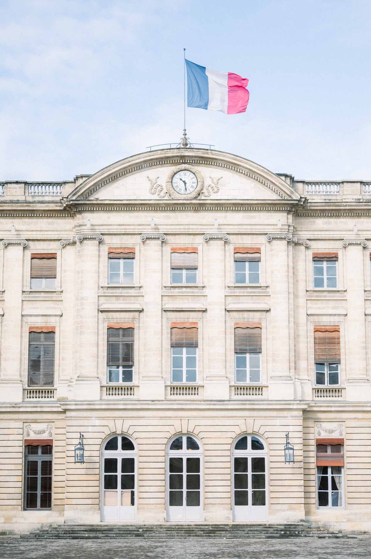 Façade de la mairie de Bordeaux et son drapeau tricolore sous un ciel bleu