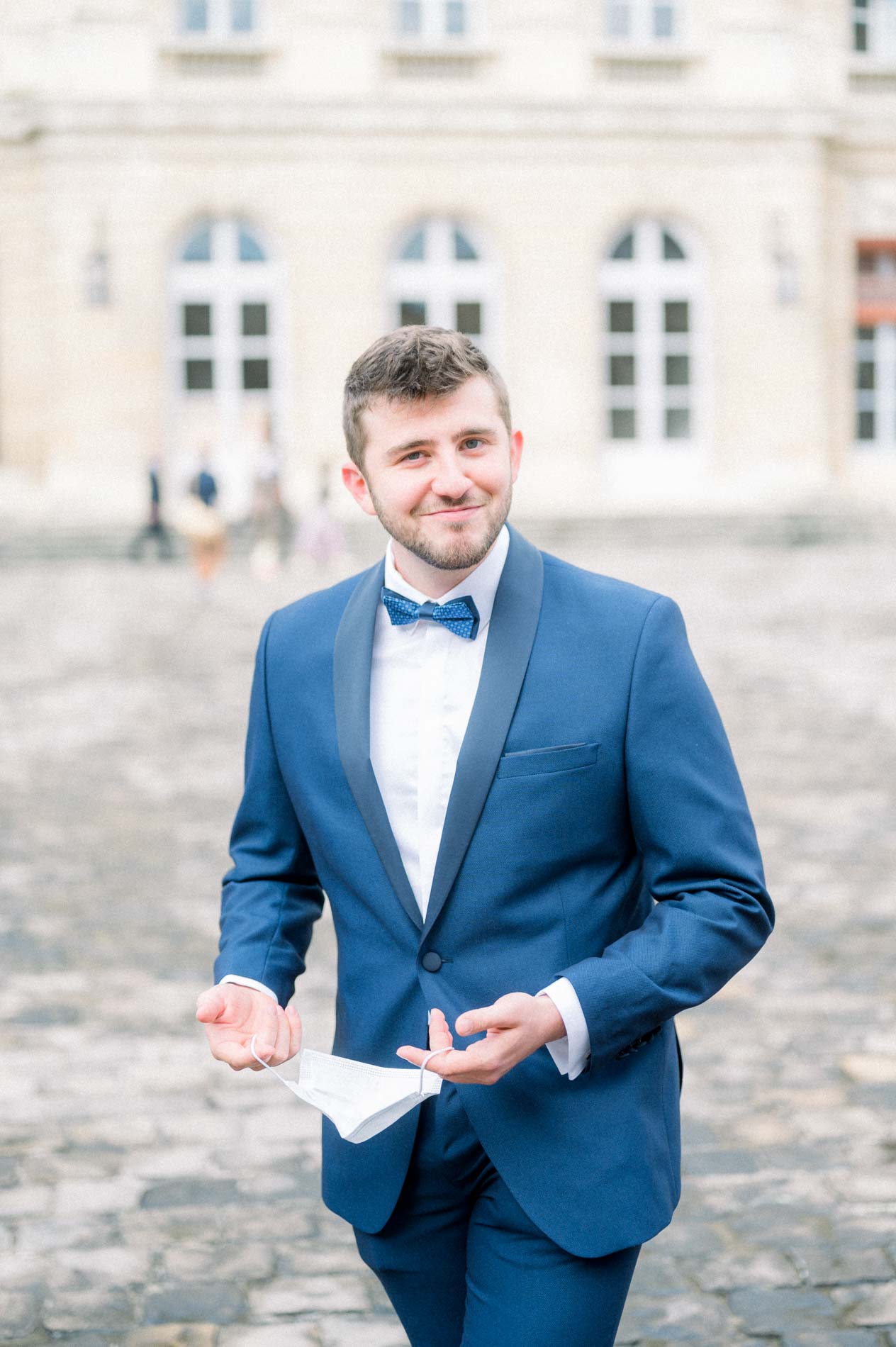 Marié souriant en costume bleu et nœud papillon dans la cour de la mairie