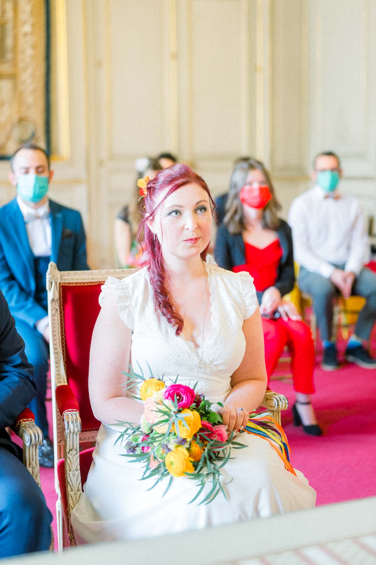 Mariée assise pendant la cérémonie civile, invités masqués derrière elle