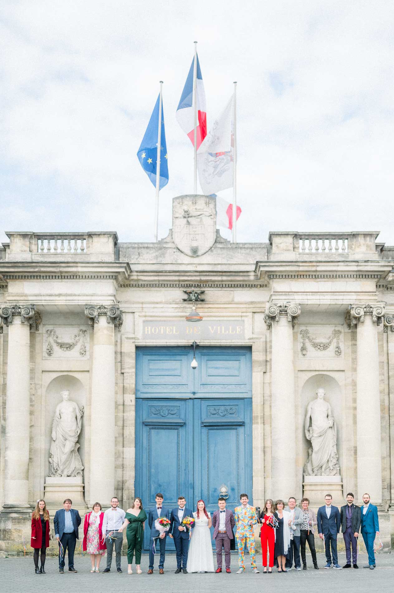 Invités alignés devant le portail bleu et les drapeaux de la mairie