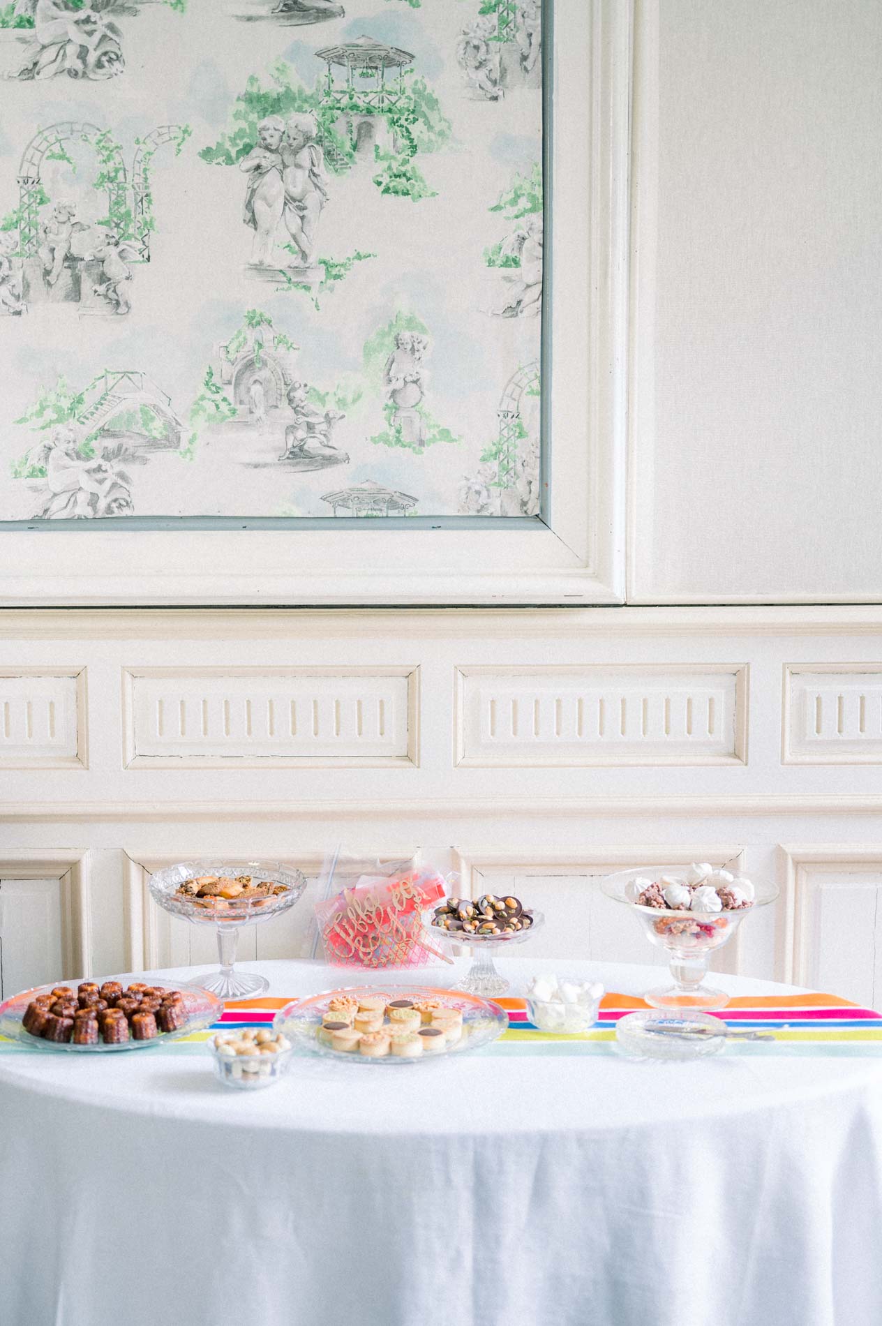 Buffet de douceurs sur nappe blanche devant un papier peint à motifs