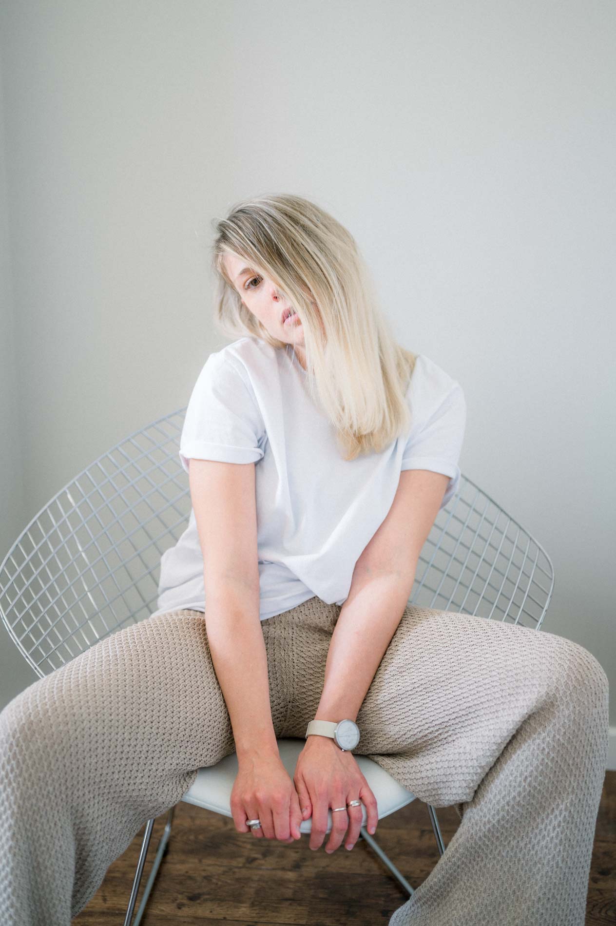 Mannequin blonde assise sur une chaise en fil métallique, regard vers le sol