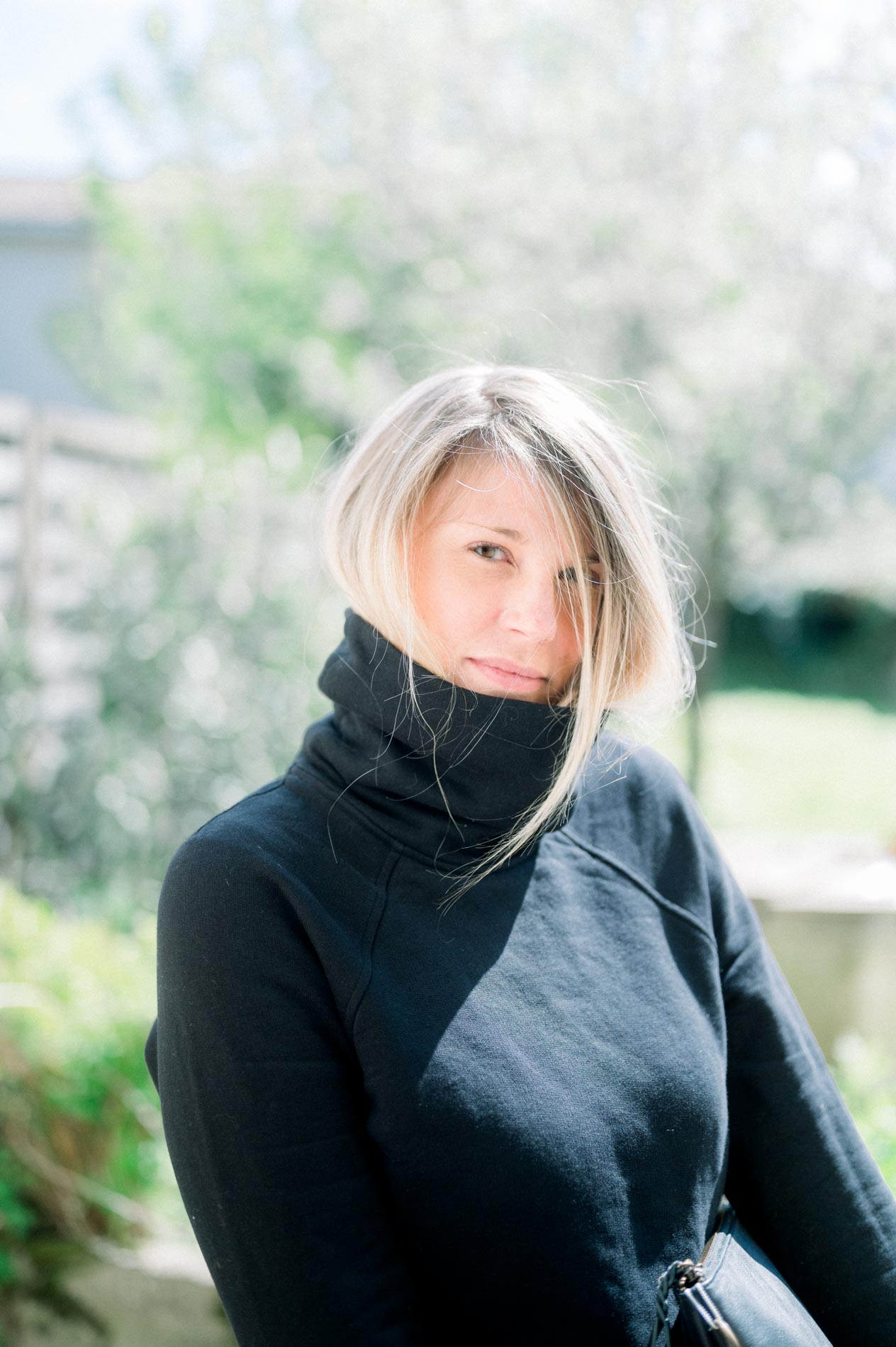 Mannequin en pull col roulé noir dans un jardin, lumière naturelle