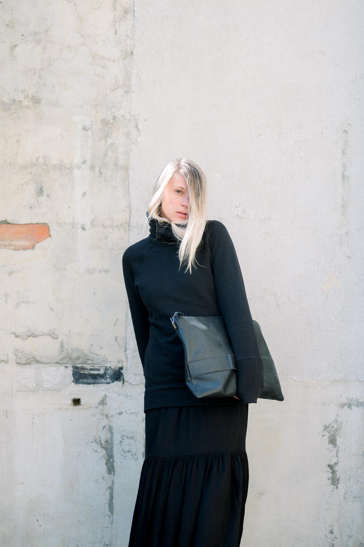 Mannequin en tenue noire et sac en cuir devant un mur patiné