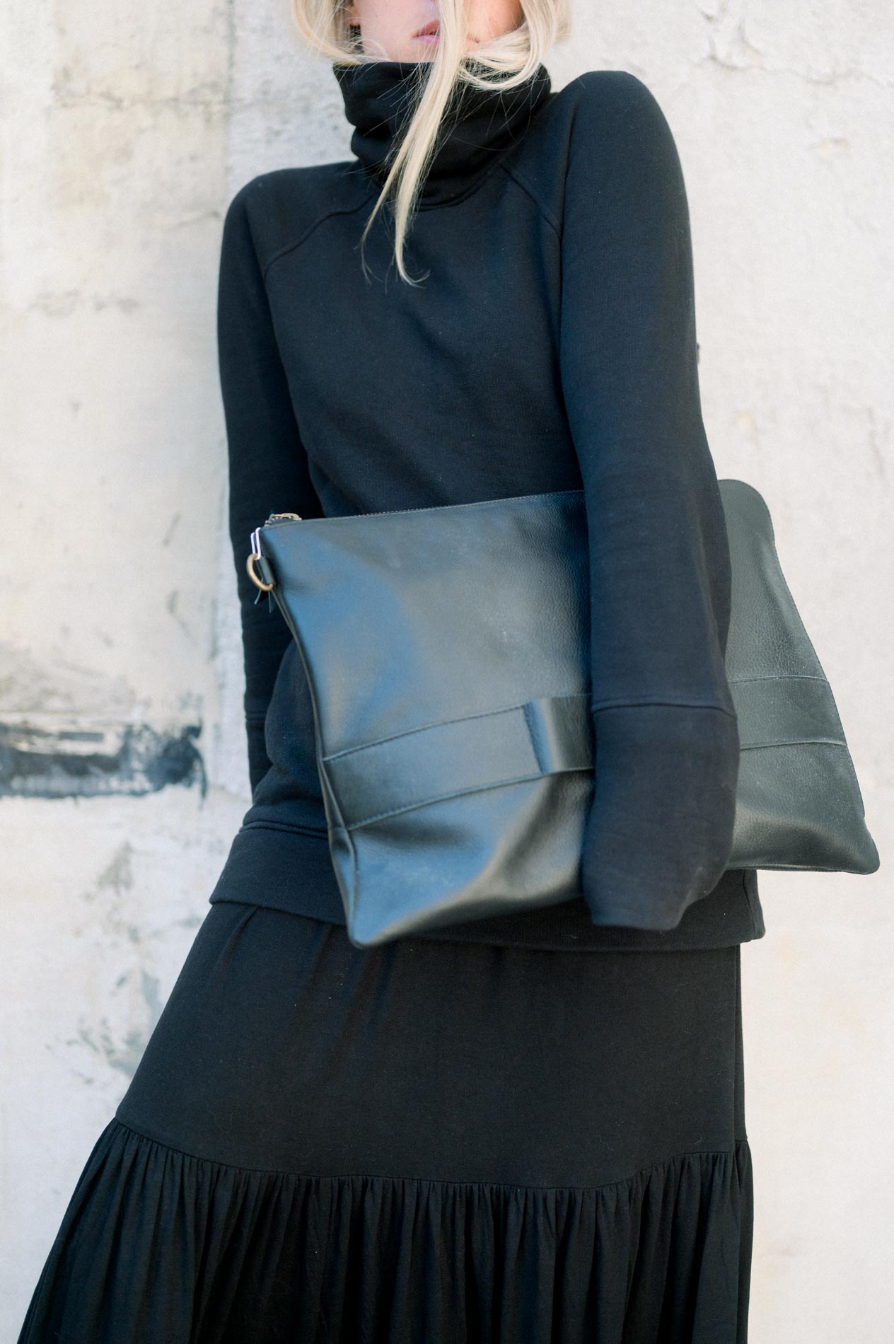 Détail d'un sac pochette en cuir noir porté avec une robe longue noire