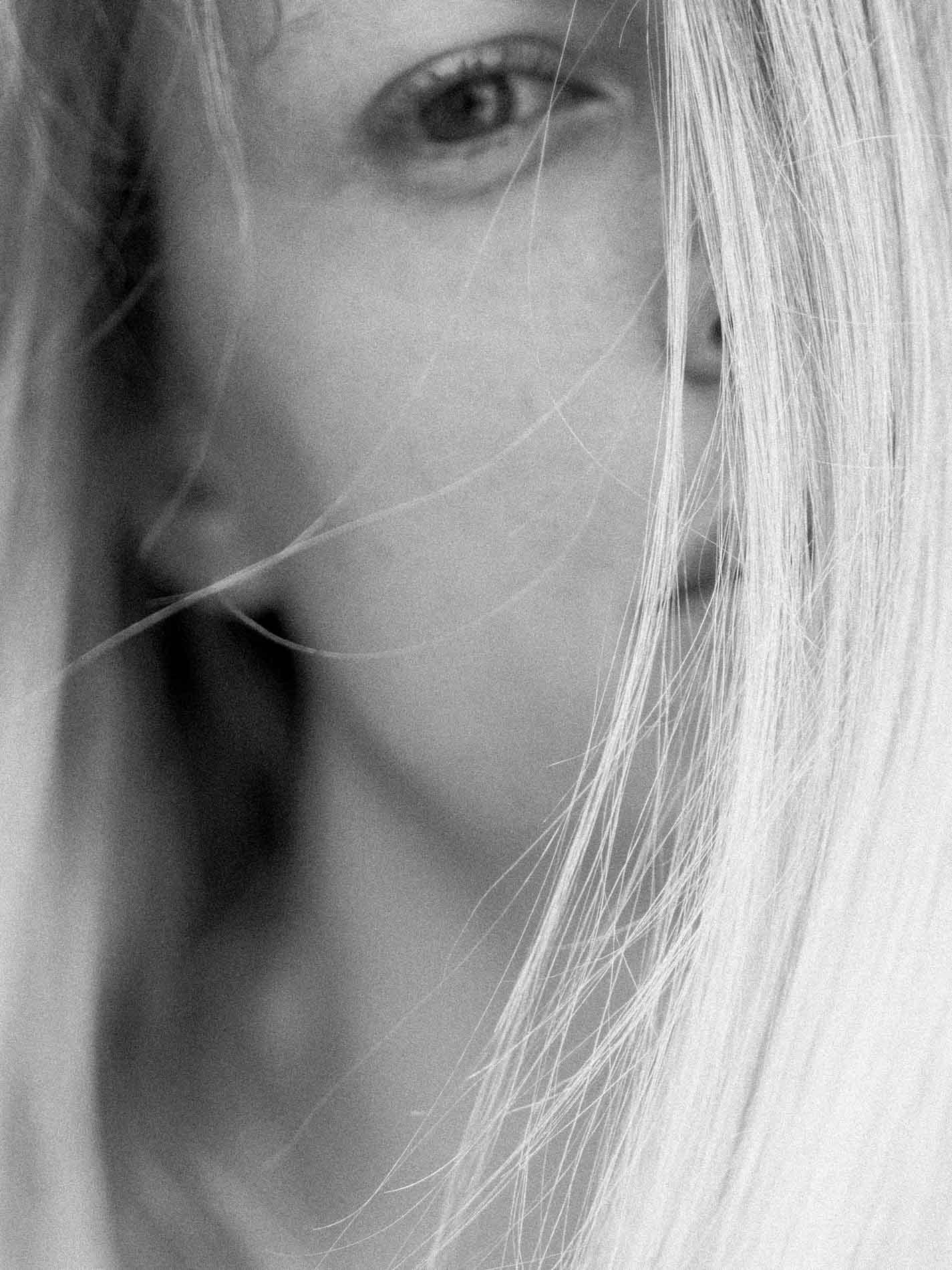 Gros plan sur le regard d'une mannequin blonde, mèche sur le visage, noir et blanc