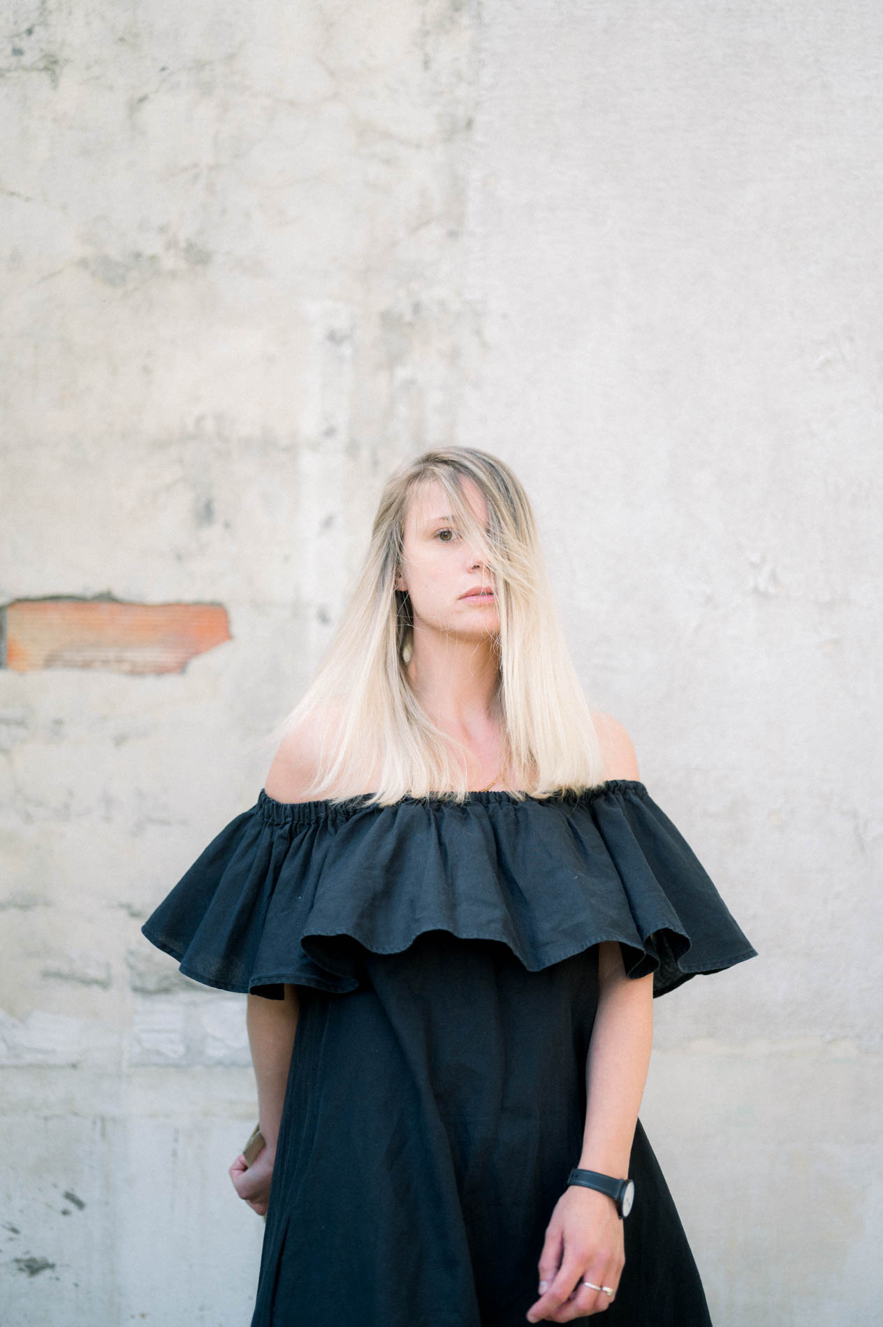 Mannequin blonde en robe noire à volants devant un mur en pierre