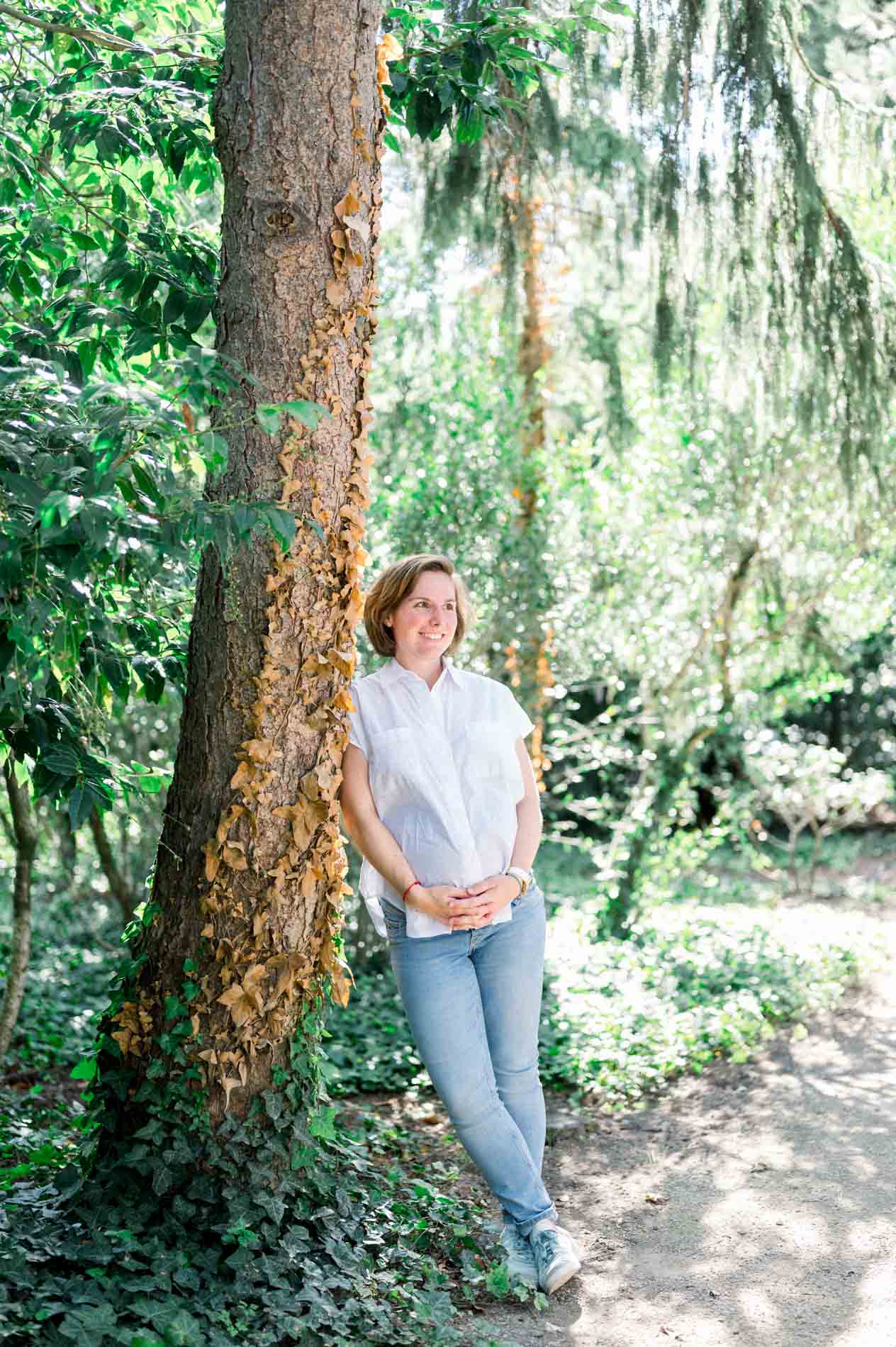 Femme enceinte adossée à un grand arbre, mains sur son ventre