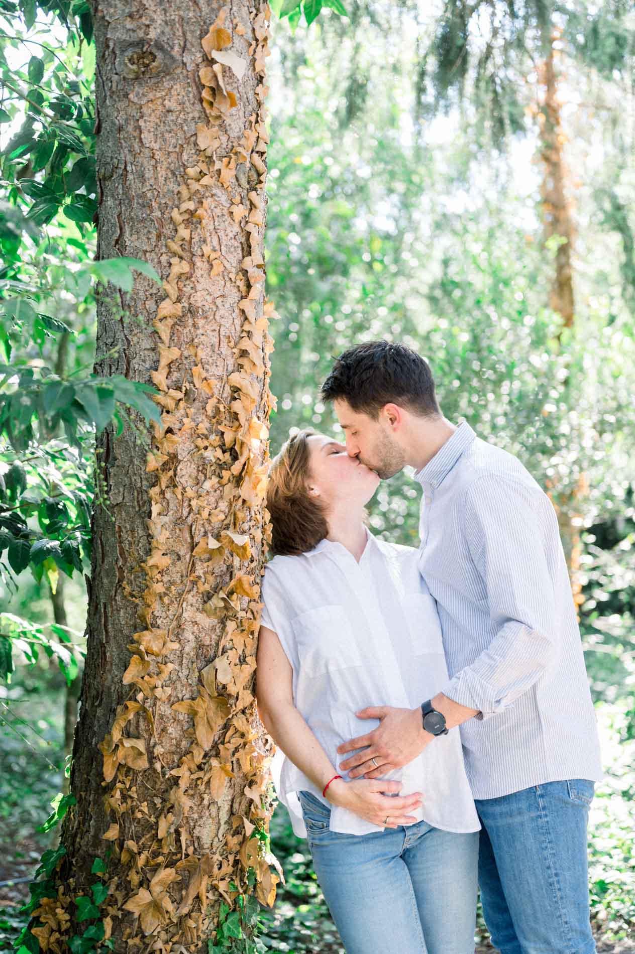 Baiser du couple contre un arbre, mains sur le ventre de grossesse