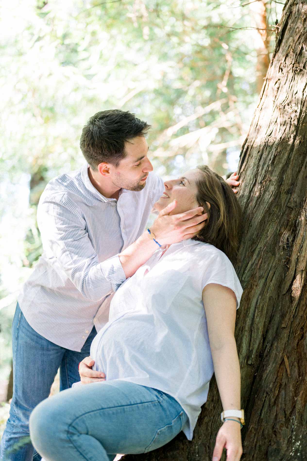 Futur papa caressant le visage de sa compagne enceinte contre un arbre