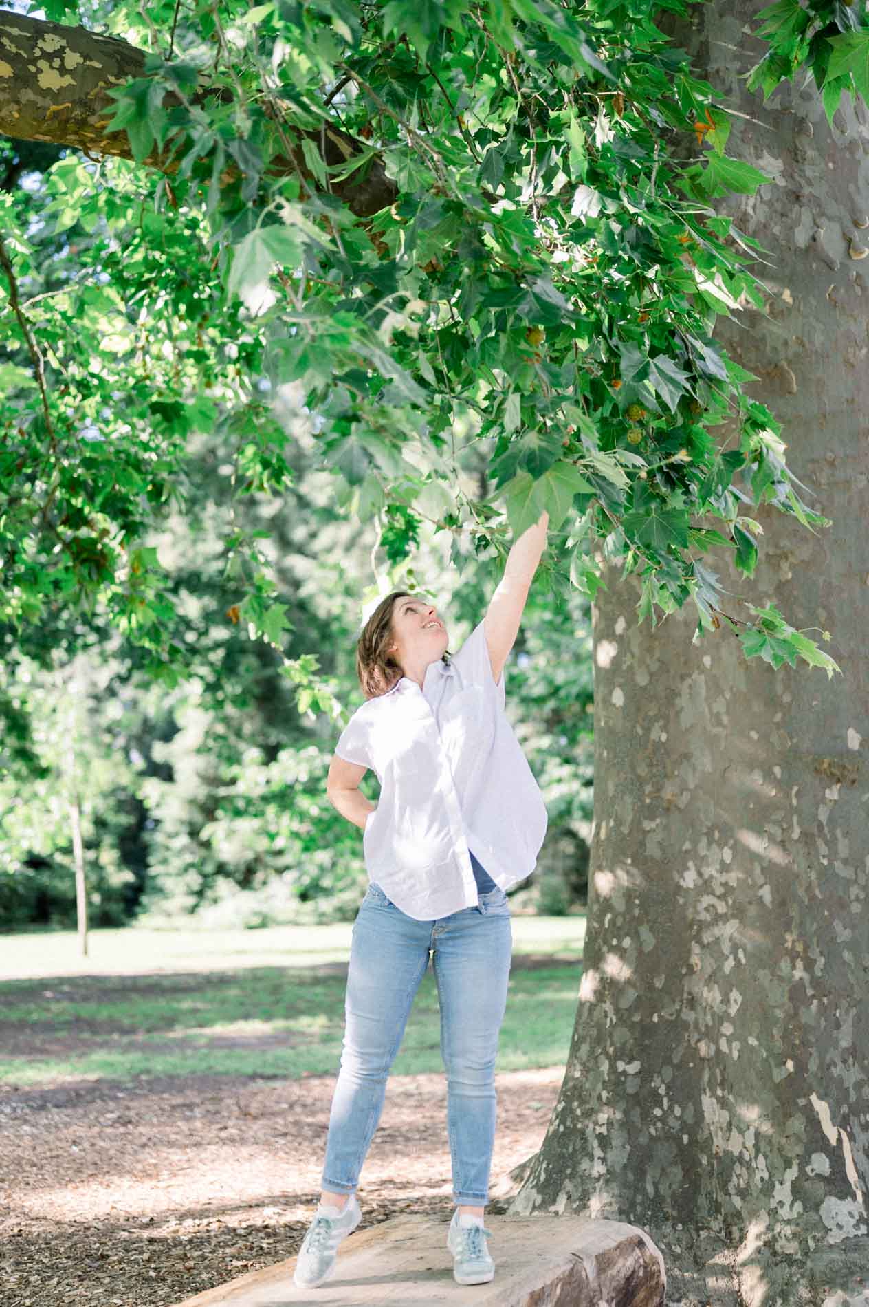 Future maman tendant le bras vers les feuilles d'un grand platane