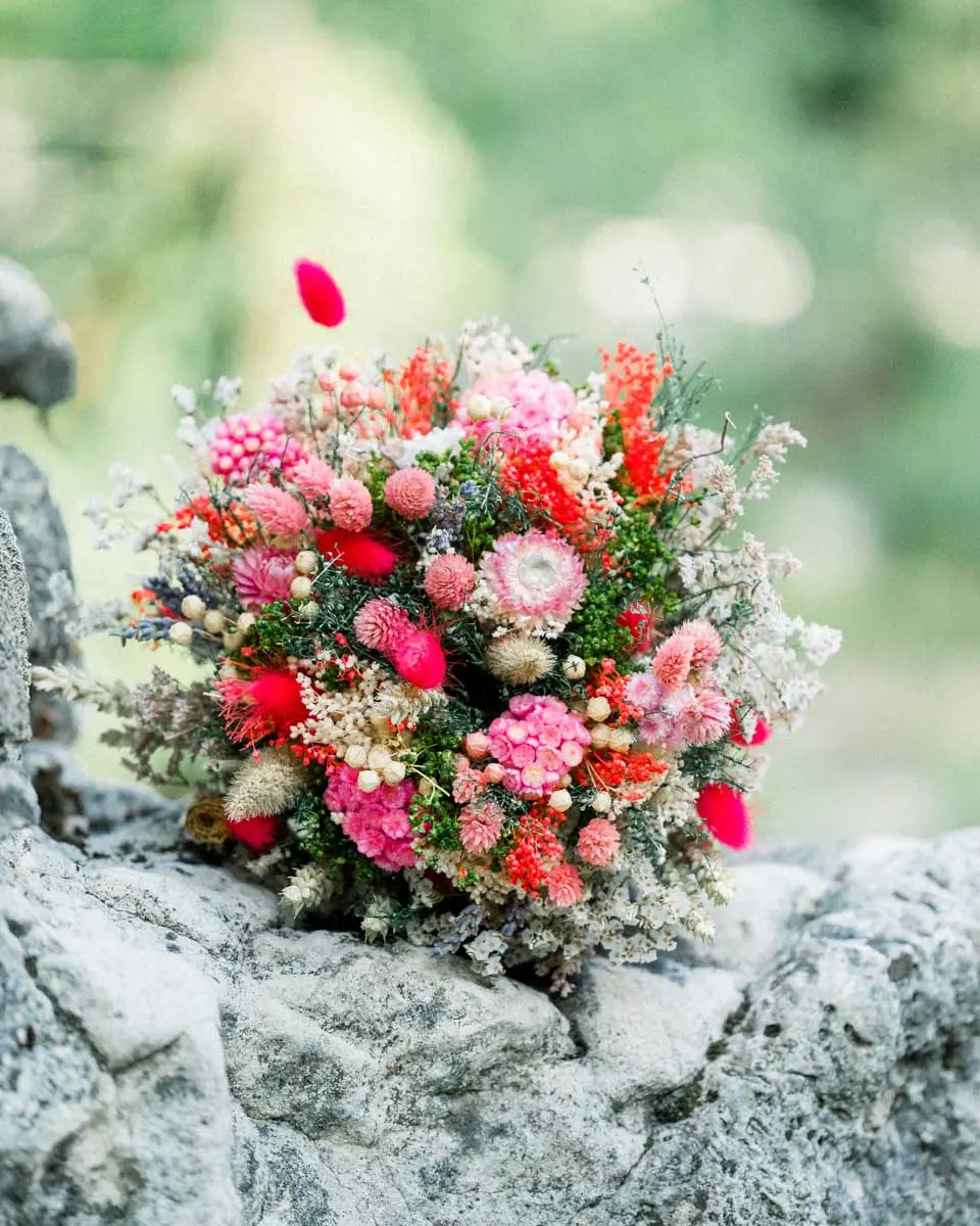 Bouquet de fleurs séchées aux tons rose et corail posé sur un rocher