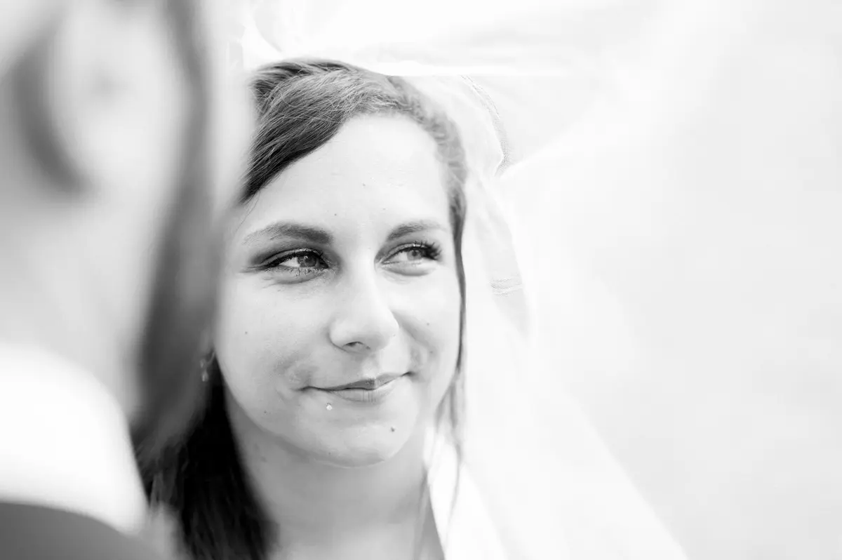 Portrait de la mariée souriante sous son voile, en noir et blanc