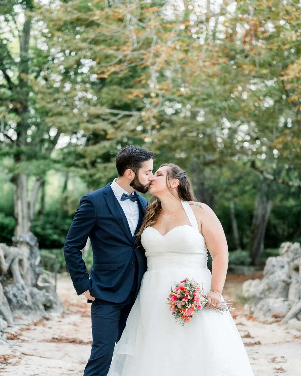 Baiser des mariés dans une allée du parc, bouquet coloré à la main