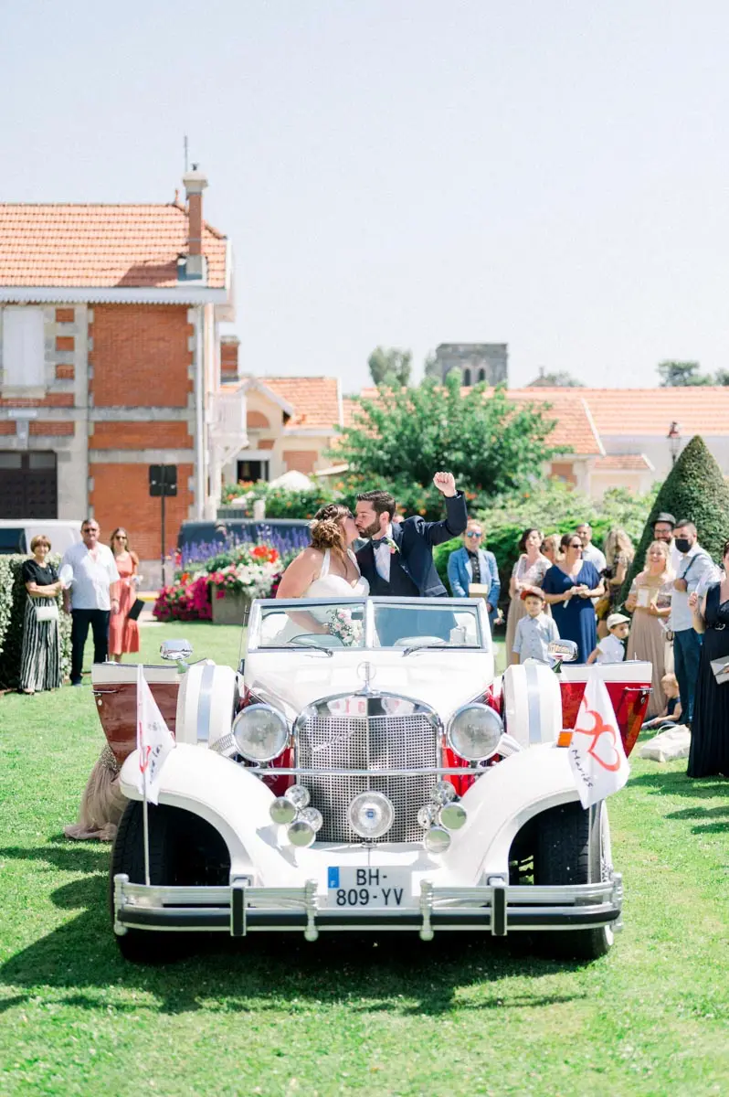 Voiture de collection blanche décorée de fleurs devant la mairie, invités autour
