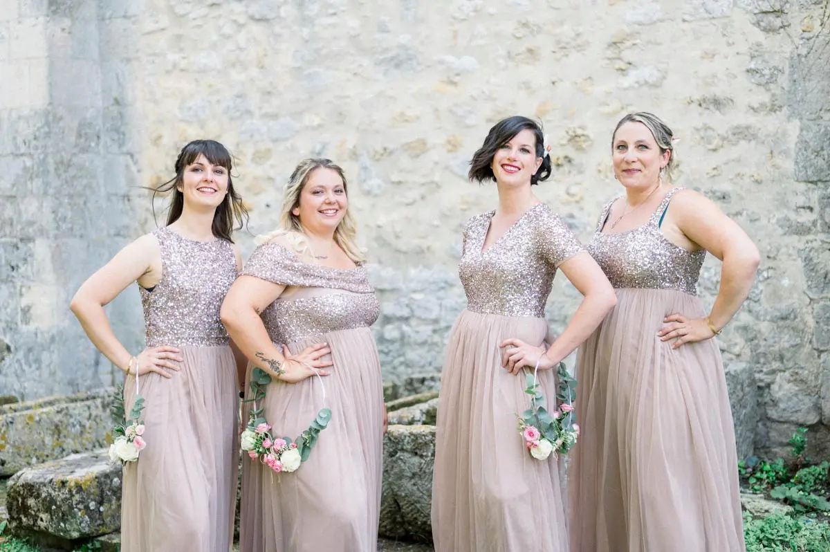 Les demoiselles d'honneur en robes à sequins nude devant un mur de pierre