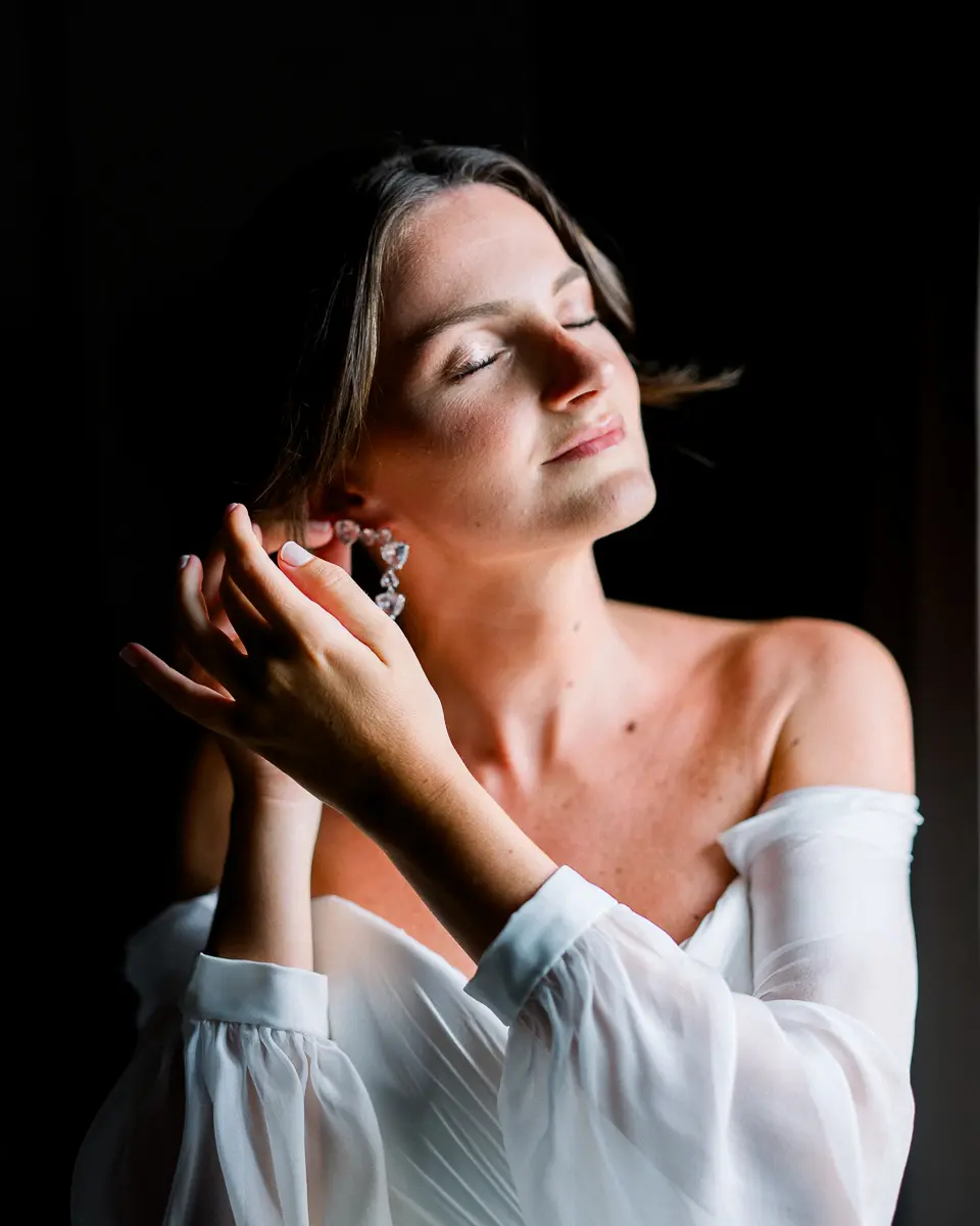 Mariée les yeux fermés attachant sa boucle d'oreille, en clair-obscur